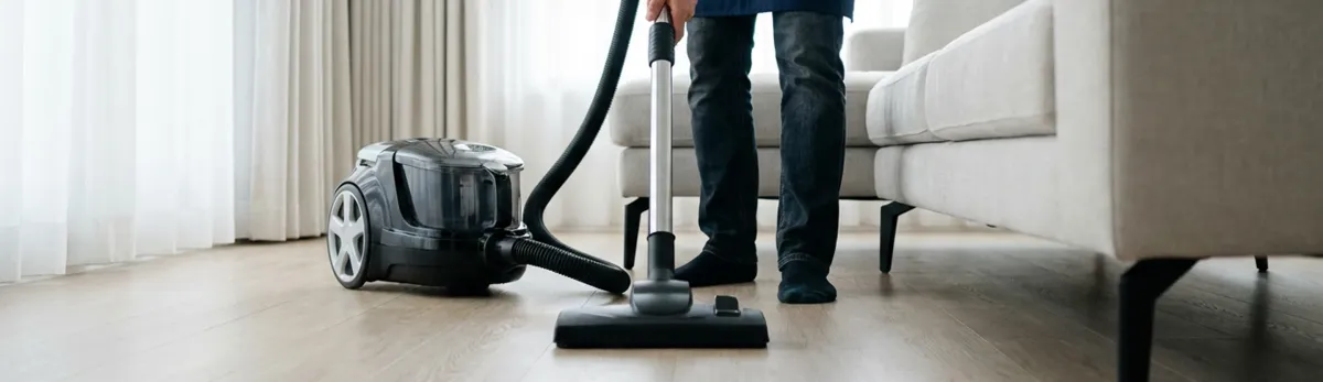 Professional house cleaner vacuuming a living room floor with a canister vacuum cleaner, Arlington, TX.